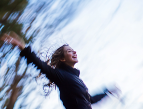 Young woman joyfully spinning outdoors with arms outstretched, captured in motion blur, embodying the freedom and happiness that comes from mindful movement in nature